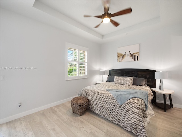 bedroom with light hardwood / wood-style flooring, ceiling fan, and a raised ceiling