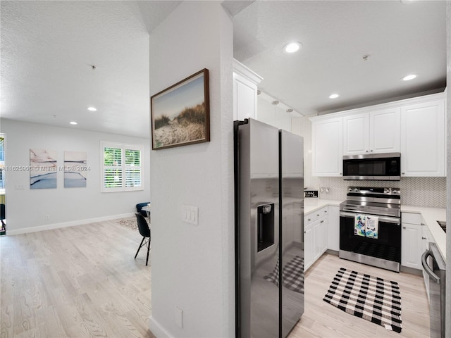 kitchen featuring appliances with stainless steel finishes, light wood-type flooring, tasteful backsplash, and white cabinets