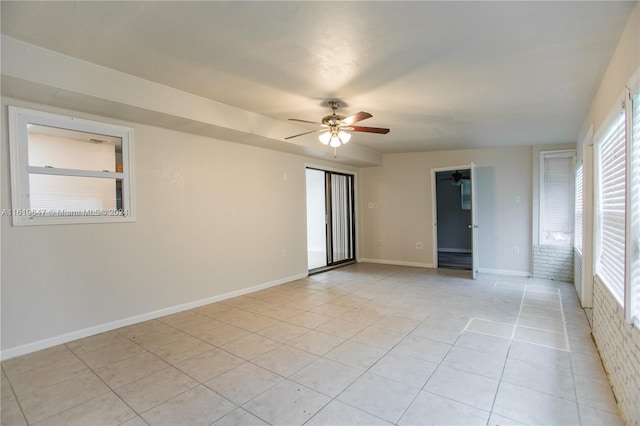 tiled empty room featuring ceiling fan and brick wall