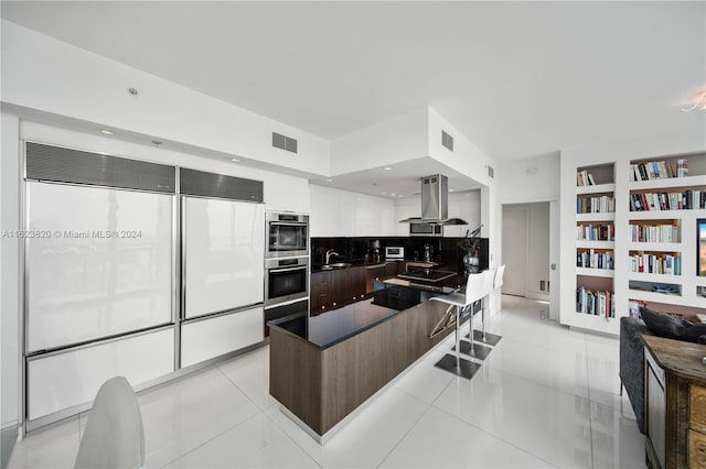 kitchen with light tile patterned floors, white cabinets, built in features, and island range hood