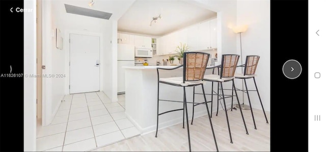 kitchen with light tile patterned floors, white cabinets, white appliances, a breakfast bar area, and kitchen peninsula