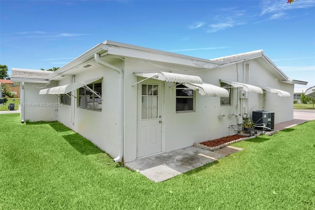 rear view of property with central air condition unit and a lawn