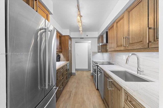 kitchen featuring appliances with stainless steel finishes, sink, decorative backsplash, wall chimney range hood, and light hardwood / wood-style flooring