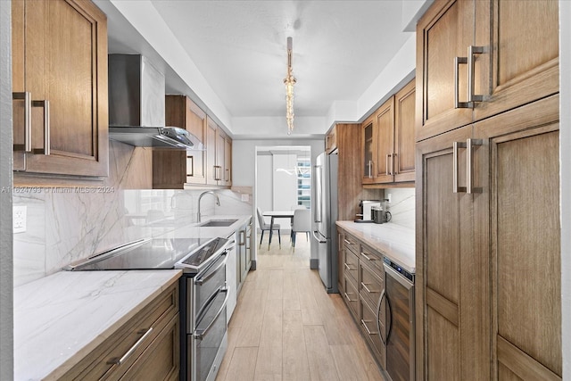 kitchen featuring sink, stainless steel appliances, tasteful backsplash, light stone counters, and wall chimney exhaust hood