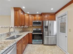 kitchen featuring tasteful backsplash, crown molding, sink, light stone countertops, and appliances with stainless steel finishes