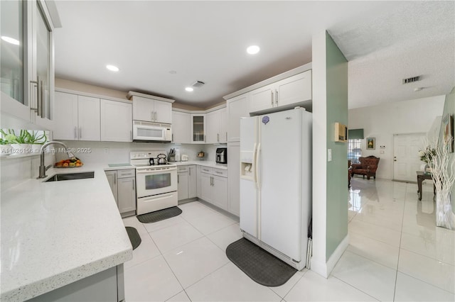 kitchen featuring a sink, white appliances, light tile patterned floors, visible vents, and glass insert cabinets