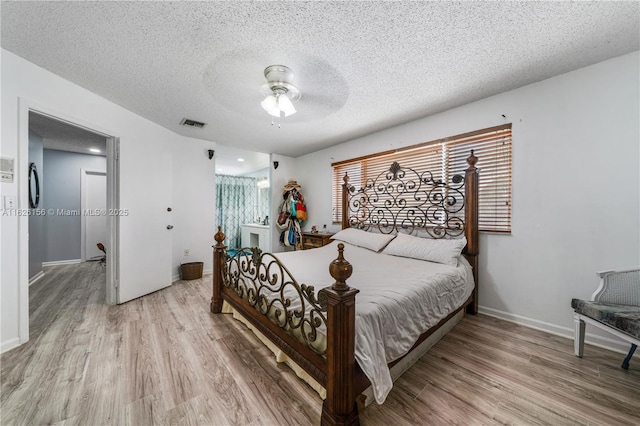 bedroom featuring a textured ceiling, baseboards, light wood-style flooring, and visible vents
