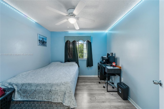 bedroom featuring baseboards, a ceiling fan, a textured ceiling, and wood finished floors