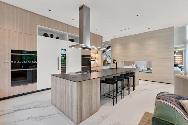 kitchen featuring sink, oven, a breakfast bar area, island range hood, and light brown cabinetry