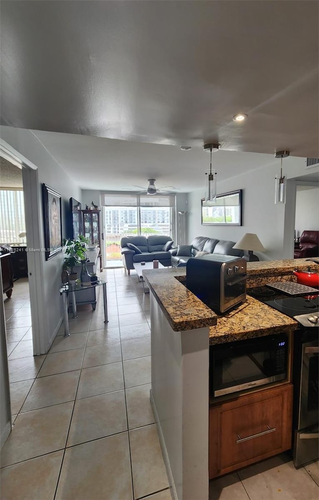 kitchen featuring stainless steel microwave, light tile patterned flooring, stone countertops, and decorative light fixtures