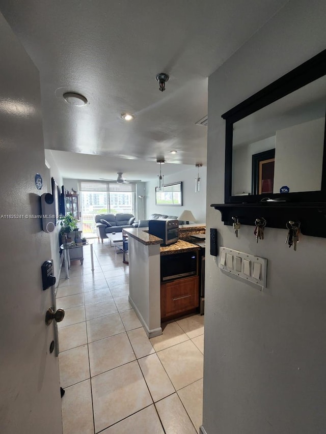 kitchen with a ceiling fan, light stone counters, built in microwave, open floor plan, and light tile patterned floors