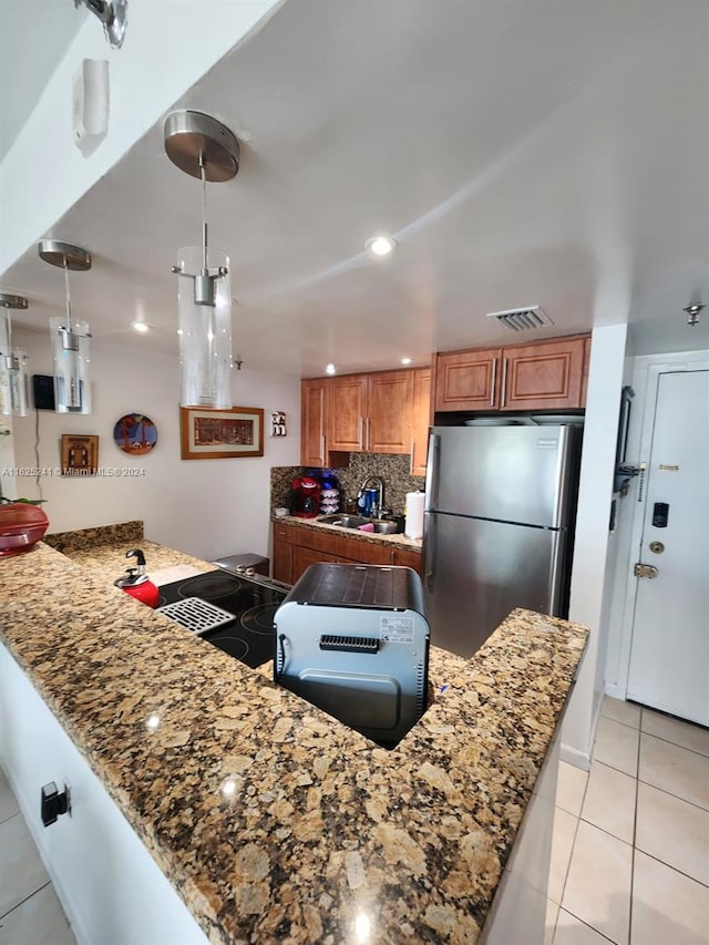kitchen featuring a sink, light tile patterned flooring, freestanding refrigerator, a peninsula, and brown cabinetry