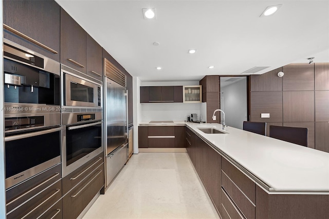 kitchen with built in appliances, sink, and dark brown cabinetry