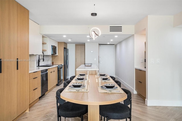 kitchen featuring tasteful backsplash, black appliances, sink, light brown cabinets, and decorative light fixtures