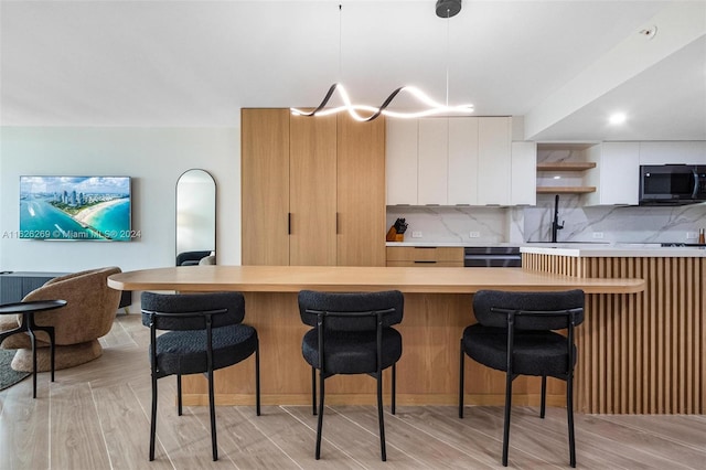 kitchen with decorative light fixtures, a kitchen bar, white cabinets, and backsplash