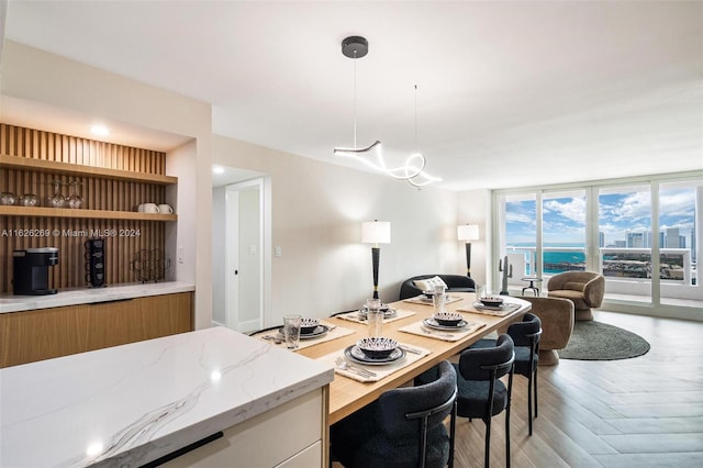 kitchen with hanging light fixtures, a water view, parquet flooring, light stone countertops, and floor to ceiling windows