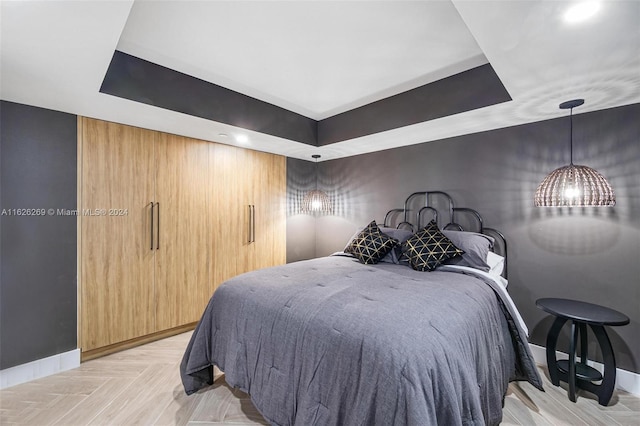 bedroom with light parquet flooring and a tray ceiling