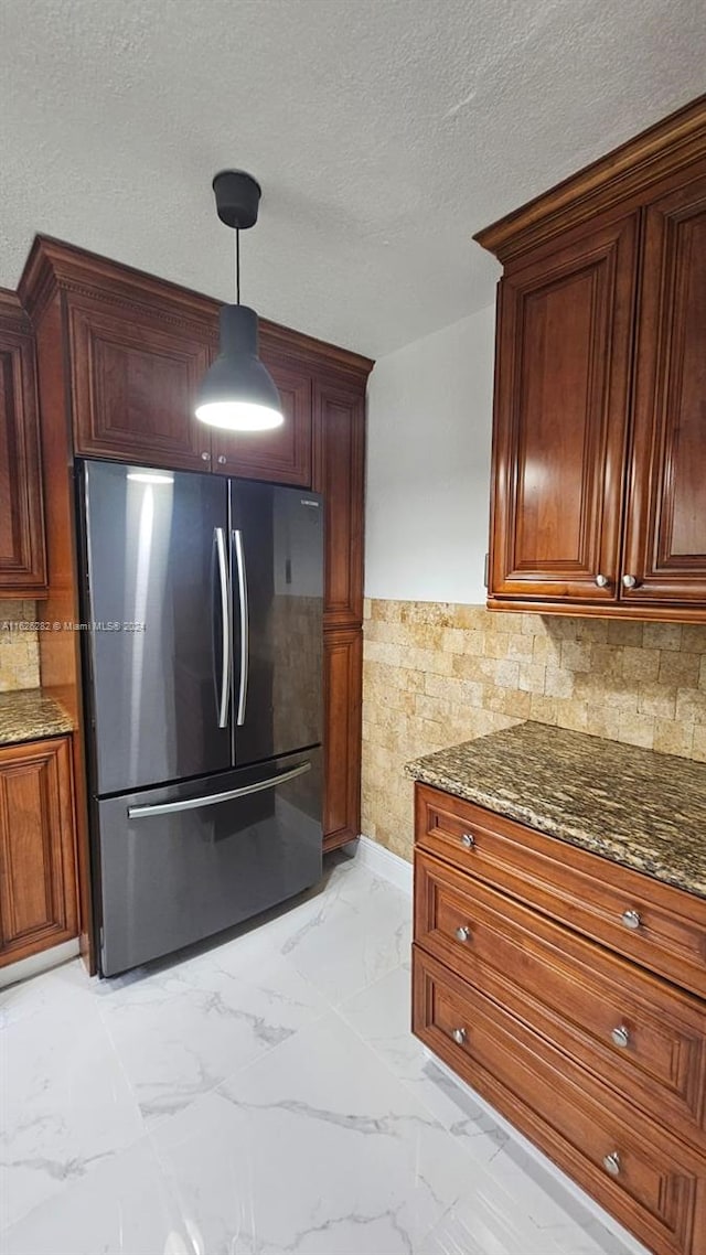 kitchen featuring backsplash, stainless steel fridge, dark stone counters, hanging light fixtures, and a textured ceiling