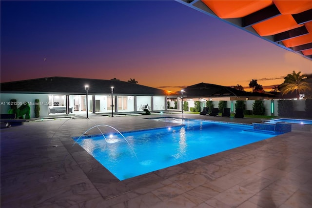 pool at dusk featuring pool water feature, a patio area, and an in ground hot tub