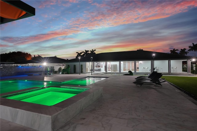 pool at dusk featuring a patio and an in ground hot tub