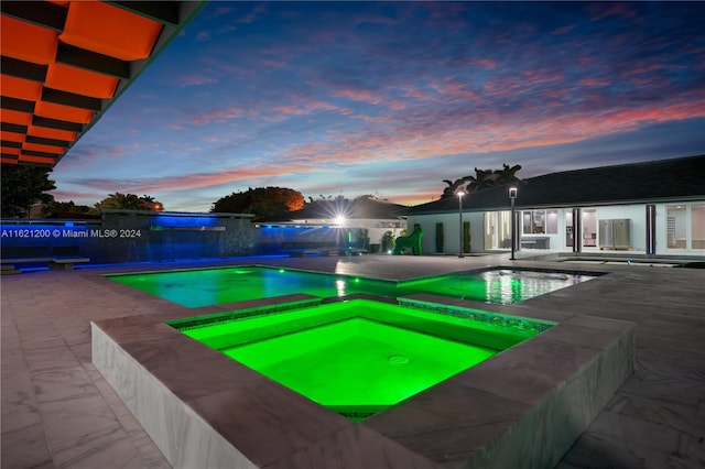 pool at dusk with a patio area and an in ground hot tub