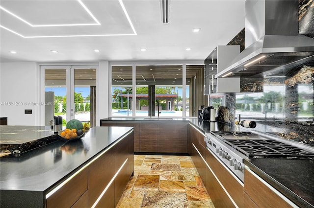 kitchen with stainless steel cooktop, french doors, wall chimney range hood, and dark stone counters