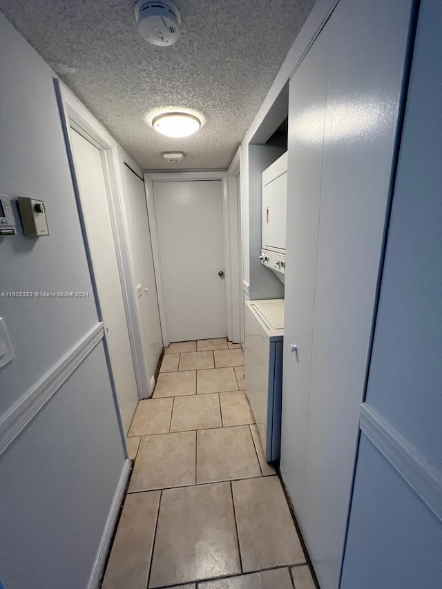 hallway with stacked washer and dryer, light tile patterned flooring, and a textured ceiling