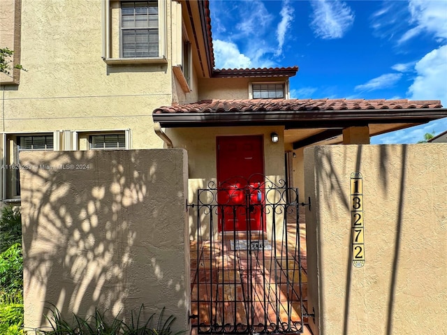 entrance to property featuring a tile roof, a gate, fence, and stucco siding