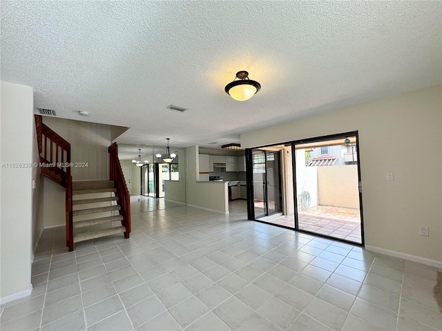 empty room featuring visible vents, stairway, light tile patterned flooring, a textured ceiling, and a chandelier