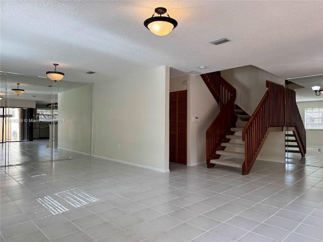 tiled empty room featuring visible vents, a textured ceiling, baseboards, and stairs