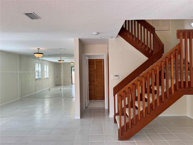 stairway with baseboards, tile patterned flooring, visible vents, and a textured ceiling