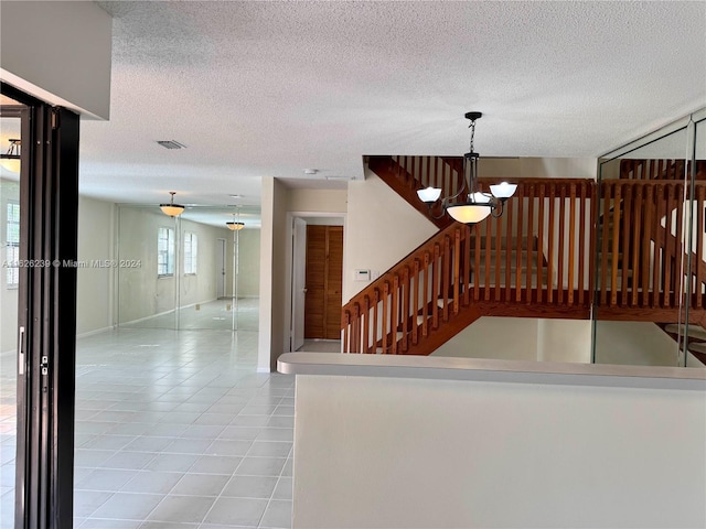 stairs with a textured ceiling, tile patterned flooring, visible vents, baseboards, and an inviting chandelier