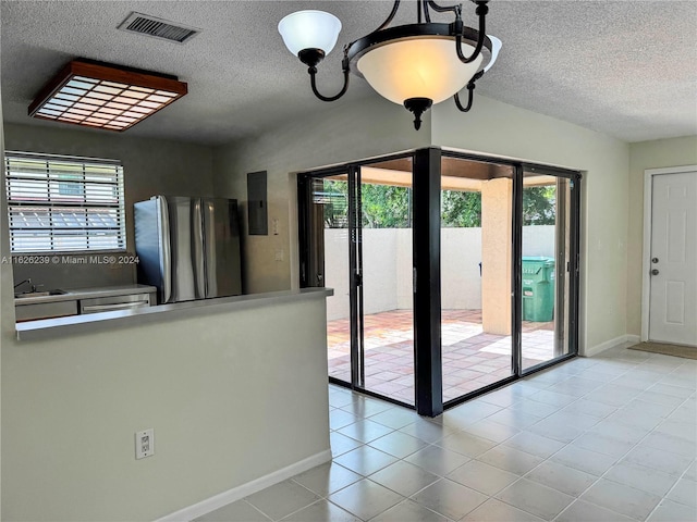 interior space with light tile patterned floors, visible vents, freestanding refrigerator, a sink, and a textured ceiling