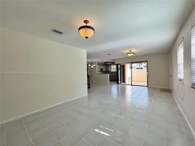 empty room featuring visible vents, a textured ceiling, baseboards, and light tile patterned flooring