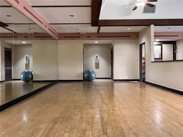 workout room featuring a textured ceiling, ceiling fan, visible vents, baseboards, and wood-type flooring