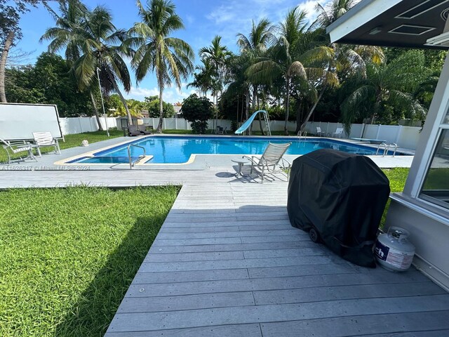 view of swimming pool featuring a water slide, a lawn, and grilling area