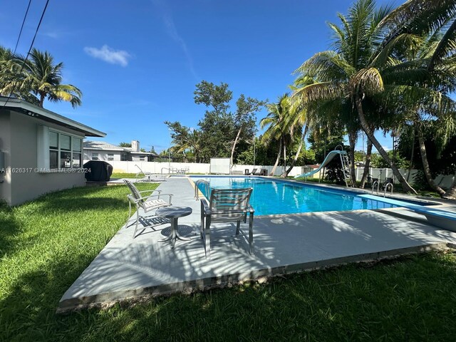 view of pool featuring a diving board, area for grilling, a water slide, and a yard