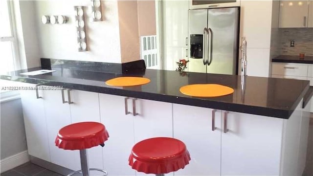 kitchen featuring white cabinetry, a breakfast bar area, stainless steel fridge, and decorative backsplash