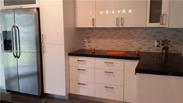 kitchen featuring stainless steel refrigerator with ice dispenser, white cabinetry, and backsplash