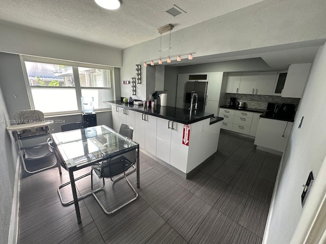 kitchen featuring hanging light fixtures, stainless steel fridge, a kitchen island with sink, decorative backsplash, and white cabinets