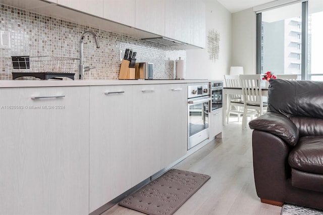 kitchen with white cabinetry, oven, light hardwood / wood-style floors, and backsplash