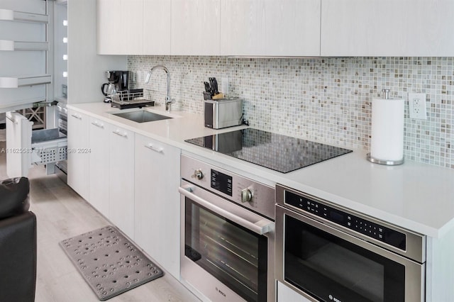 kitchen featuring sink, white cabinets, oven, backsplash, and black electric stovetop