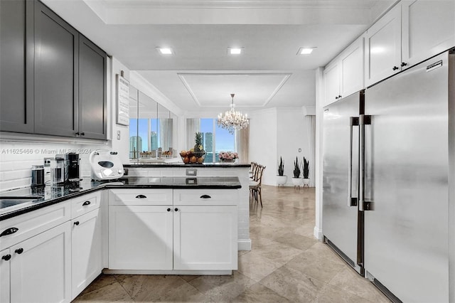 kitchen with high end refrigerator, an inviting chandelier, light tile patterned floors, kitchen peninsula, and white cabinets