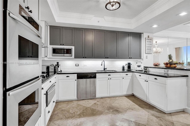 kitchen featuring dark countertops, appliances with stainless steel finishes, a tray ceiling, and a sink