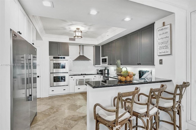 kitchen with ornamental molding, backsplash, a peninsula, appliances with stainless steel finishes, and wall chimney exhaust hood