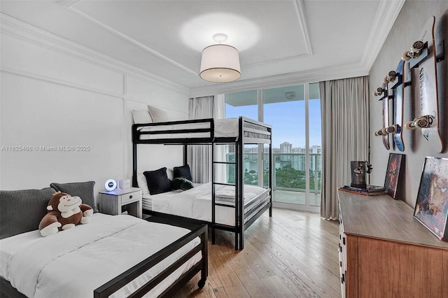 bedroom featuring light wood-type flooring, a city view, expansive windows, a tray ceiling, and crown molding