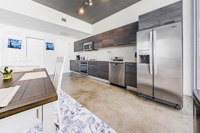 kitchen with rail lighting, appliances with stainless steel finishes, sink, and dark brown cabinetry