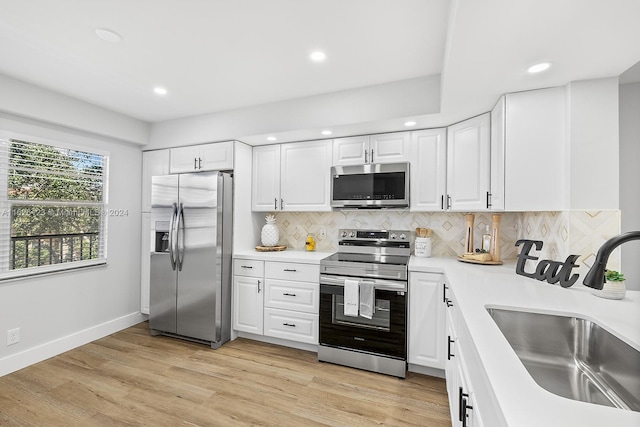 kitchen with white cabinets, sink, appliances with stainless steel finishes, light hardwood / wood-style floors, and decorative backsplash