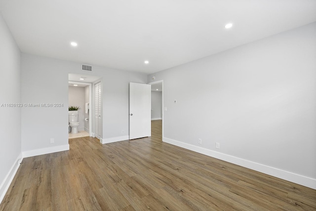 unfurnished bedroom with ensuite bath and wood-type flooring