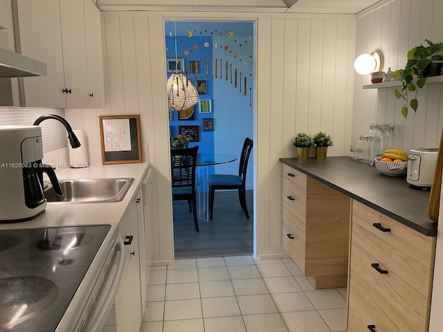 kitchen with wood walls, white range with electric cooktop, light tile patterned floors, and sink